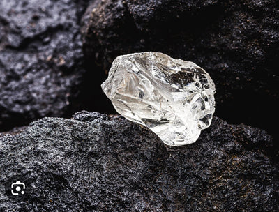 Rough uncut diamond resting on dark kimberlite rock, representing De Beersâ new kimberlite field discovery in Angola
