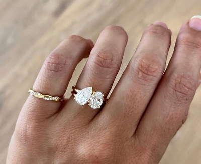A hand with a Toi et Moi engagement ring, featuring an oval and pear shaped diamond set side by side in a modern two-stone design.