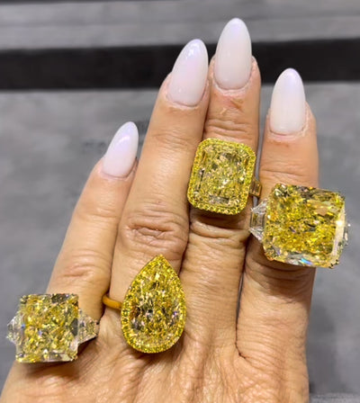 A close-up of a four large yellow diamond engagement rings on a womanâs hand, featuring a vivid canary yellow diamond set in yellow gold.