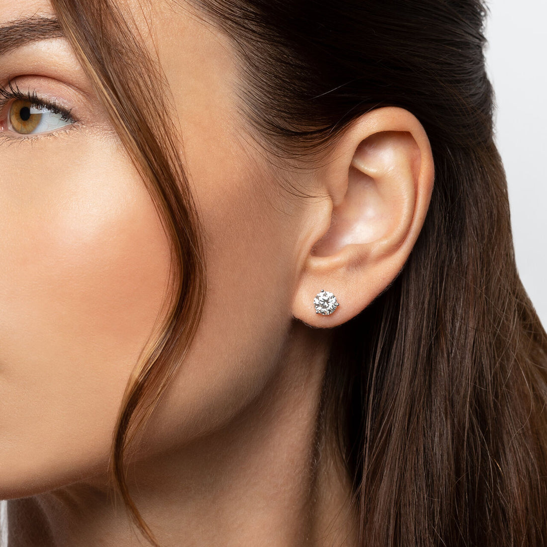 Close-up of a womanâs ear wearing a classic round brilliant diamond stud earring in a simple prong setting.