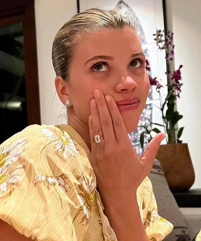 Close-up of Sofia Richie wearing an emerald cut diamond solitaire engagement ring in yellow gold