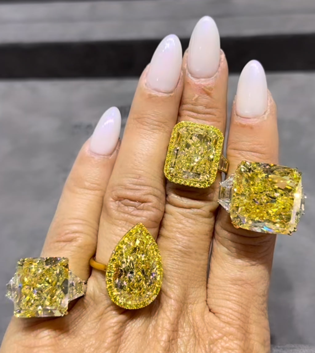 A close-up of a four large yellow diamond engagement rings on a woman’s hand, featuring a vivid canary yellow diamond set in yellow gold.